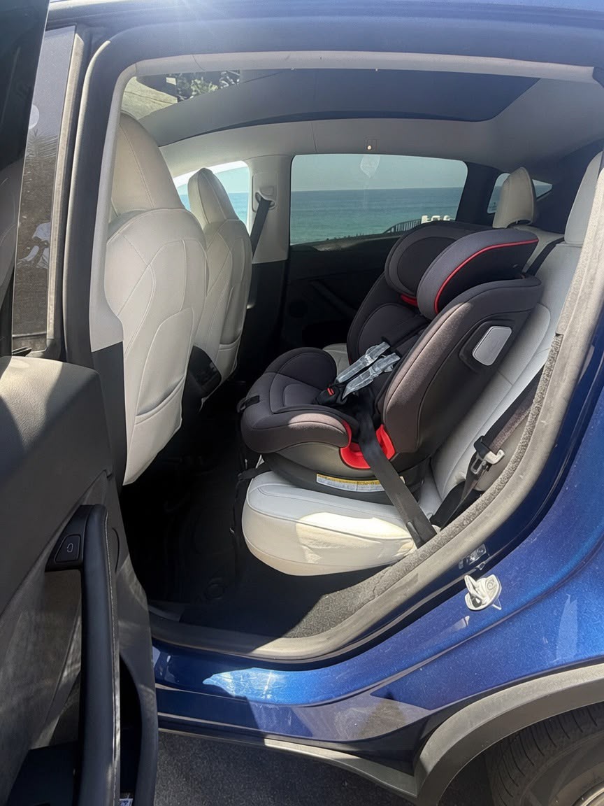 Certified child seat fitted in the white leather rear seat of the blue Tesla